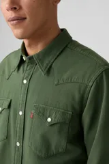Camisa de hombre verde militar, estilo western, con cuello clásico, cierre de botones a presión blancos, dos bolsillos con solapa en el pecho y costuras decorativas en los hombros.