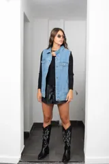 Chaleco de jean largo con corte oversize, cierre frontal con botones metálicos, bolsillos laterales y bolsillos superiores con solapa.