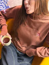 Buzo de algodón rústico color crema, con cuello redondo, corte boxy y costuras externas visibles. Presenta puños con abertura para el pulgar y un bordado pequeño en el pecho.