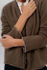 Saco básico de punto color marfil, confeccionado en lambswool, con corte entallado tipo chaquetita. Destaca por detalles de blonda tejida en los puños y a lo largo de la abertura frontal, con bordes en color contrastante.