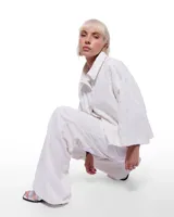 Pantalón de denim color blanco con patrón caliza, corte sastrero de pierna ancha, tiro alto, cierre frontal invisible, pretina cruzada y bordado negro del logo Temblad en la parte trasera.