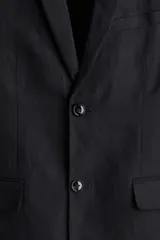 Blazer negro de lino liviano con solapas de muesca finas y ojal decorativo. Presenta botonadura sencilla con dos botones, bolsillo superior, bolsillos delanteros con solapa y dos bolsillos interiores. Tiene botones decorativos en los puños y abertura doble en la parte trasera. Corte ajustado y forrado.