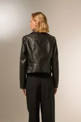 Chaqueta corta de cuero sintético negro con cuello solapa con tachas plateadas, cierre cruzado con cremallera, bolsillos con cremallera y corte holgado.