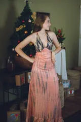 Vestido largo con estampado tie-dye en tonos violeta y fucsia, escote en V con detalles bordados dorados, cut-outs laterales bajo el busto y tirantes finos que se cruzan y atan en la espalda.