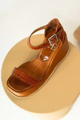 Sandalias de plataforma negra con diseño de puntera cuadrada, tira delantera fina y pulsera ajustable al tobillo con hebilla metálica. Presentan una textura tipo reptil en la parte posterior y una base de plataforma sólida.