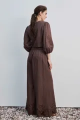 Pantalón largo negro de corte ancho y holgado, con bolsillos laterales y detalle de bordado calado en el ruedo.
