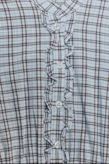 Vestido corto de algodón con estampado de cuadros en tonos celeste, blanco y negro. Presenta cuello redondo, manga corta abullonada, talle ajustado con smock elástico y falda con volantes superpuestos. Tiene un detalle de volado en el frente con botones.