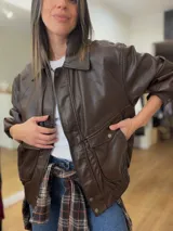 Campera de efecto cuero en color marrón chocolate, con diseño de corte relajado, cierre frontal, bolsillos amplios con solapa y terminaciones elastizadas en puños y ruedo.