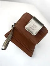 Billetera compacta de cuero texturizado color marrón, con solapa frontal en cuero metalizado dorado que presenta un grabado de búho. Incluye cierre lateral y correa de muñeca a juego.