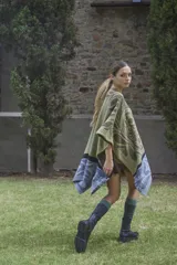 Ruana tejida en lana lambswool con diseño de bloques de color y tramas geométricas. Presenta cierre frontal con doble cursor y tiradores de cuero, permitiendo diferentes formas de uso.