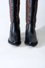 Bota texana de cuero negro con apliques de cuero marrón en los laterales y pespuntes en color crema. De caña media/alta y taco bajo. Diseño calado con motivos geométricos.