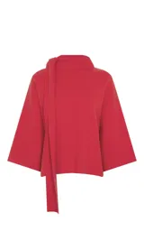 Blusa de punto color rojo con diseño de cuello asimétrico que incorpora una bufanda integrada. Presenta mangas anchas de largo tres cuartos y un corte holgado.