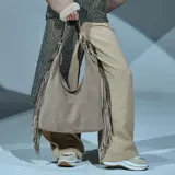 Cartera hobo de cuero color taupe, con diseño slouchy y flecos largos en los laterales. Cuenta con asa para el hombro y herrajes metálicos.