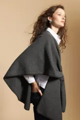 Poncho de tejido suave color beige con diseño envolvente y terminaciones con costuras decorativas en contraste color negro. Presenta un detalle de lazo frontal integrado.