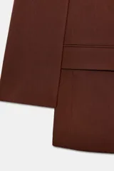 Blazer marrón de cuello solapa con muescas, manga larga y bolsillos de vivo con solapa. Cierre frontal con un botón.