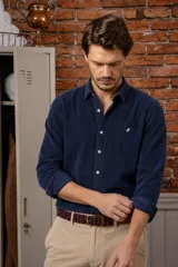 Camisa azul marino de pana, de corte slim fit, con cuello clásico, botones delanteros claros y detalle de ave bordada en el pecho.