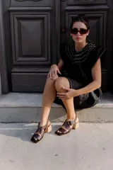 Sandalias de cuero negro con textura de reptil, diseño de punta cuadrada y taco bloque de madera. Presentan tiras cruzadas en el empeine y una hebilla metálica grande decorativa.