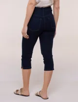 Pantalón capri de jean azul con calce ajustado, tiro alto, cinco bolsillos, cierre frontal con botón y pequeños tajos en los ruedos.
