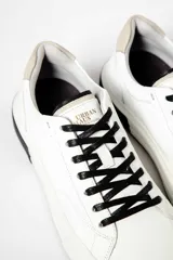 Zapatillas urbanas blancas de cuero con cordones negros, suela blanca y detalle negro en el talón.