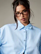Camisa de rayas verticales celestes y blancas, con cuello clásico, mangas largas abullonadas con puños abotonados y espalda abierta con lazo regulable.