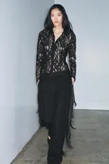 Camisa de manga larga confeccionada en encaje negro con patrón floral. Presenta cuello solapa de tejido liso negro y cierre frontal de botones. El bajo del ruedo y los puños tienen terminación de encaje festoneado.