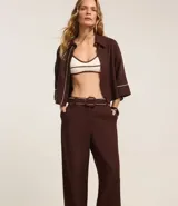 Pantalón wide leg de cintura alta color marrón, confeccionado en viscolino con 15% de lino, con trabillas en la cintura y vieses contrastantes en las barras. Incluye cinturón de tejido con hebilla metalizada de efecto martillado.