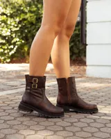 Botas de caña media color marrón con acabado desgastado, confeccionadas en cuero. Presentan una suela chunky dentada, cierre lateral y dos correas decorativas con hebillas metálicas en el lateral exterior.