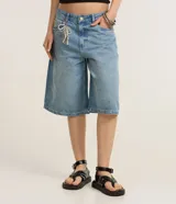 Bermuda tipo jorts de tiro medio, confeccionada en denim de algodón color azul claro. Presenta un corte holgado que llega por debajo de la rodilla, con trabillas en la cintura, bolsillos laterales y traseros, y un detalle de cordón decorativo en la parte frontal.