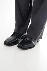 Zapato de charol negro de cuero vacuno con textura grabada tipo reptil, punta cuadrada y cordones al tono.