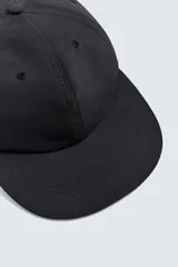 Gorra de seis paneles color negro, confeccionada en tejido técnico, con visor plano y ajuste trasero.