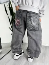 Pantalón de jean estilo baggy, color gris lavado, con bordados decorativos en los bolsillos traseros. Presenta un diseño holgado y relajado.