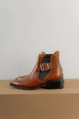 Botín negro de charol con punta cuadrada y hebilla metálica decorativa.