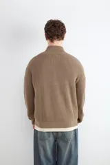 Chaqueta de punto de algodón color marrón, con cuello alto y cierre frontal con cremallera.