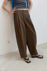 Pantalón de tiro alto con diseño balloon, presenta pliegues frontales, trabillas para cinturón, bolsillos laterales y cierre frontal con cremallera y botón.