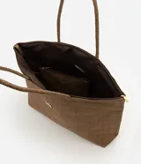 Cartera amplia confeccionada en fibra de papel, de color beige, con asas de hombro, cierre superior y detalle metálico dorado claro en el frente.
