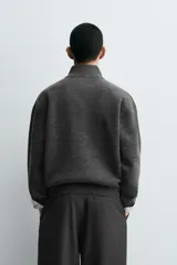 Jersey de punto de corte regular, color gris oscuro, con cuello subido y cierre frontal de cremallera. Presenta mangas largas y acabados en rib en puños y ruedo.