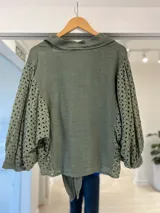 Camisa verde militar de lino, con mangas abullonadas y paneles laterales de broderie, cuello camisero, cierre frontal de botones y detalle de lazo para atar en el frente.