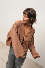 Blusa marrón de corte crop, escote en V y mangas largas anchas. Cierre frontal con lazos.