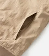 Campera tipo bomber de sarga color beige, con cuello inglés, cierre frontal de cremallera y puños y cintura ajustados con elástico en tono contrastante.