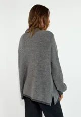 Sweater de tejido de punto en color azul marino, con cuello redondo, mangas largas con puños acanalados y ajuste holgado. Presenta un pequeño aplique decorativo en el ruedo.