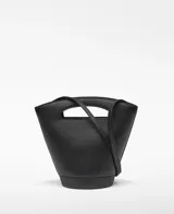 Bolso tipo capazo pequeño de piel ovina negra, con base cilíndrica y cuerpo que se ensancha hacia arriba. Presenta un asa corta troquelada en la parte superior y una correa larga ajustable y extraíble para llevar al hombro o cruzado. Tiene un compartimento principal con cierre de cremallera y el logo grabado en dorado en la parte inferior frontal.