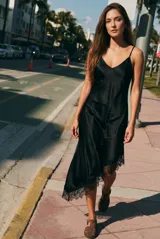 Vestido midi de satén negro con escote en V y tirantes finos. Presenta un diseño asimétrico en el ruedo con detalle de encaje aplicado.