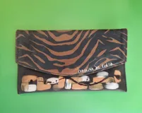 Sobre de mano rectangular de cuero, con solapa combinada en diseño animal print de cebra y detalles pintados a mano en la parte inferior. Cuenta con cierre de imán y compartimentos internos.