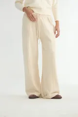 Pantalón de punto color crema, de corte recto y holgado, con cintura elástica y cordón ajustable. Presenta costuras verticales decorativas a lo largo de las piernas.