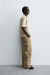 Pantalón cargo de denim lavado negro, corte relajado y tiro medio. Presenta múltiples bolsillos cargo con solapa y detalle de cierre en las perneras, además de bolsillos de vivo traseros. El bajo es ajustable con trabilla.