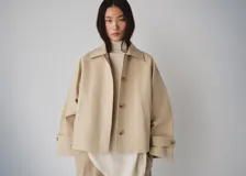 Chaqueta de corte recto y holgado color beige, con cuello clásico, cierre frontal de botones marrones, bolsillos de ojal laterales y puños ajustables con presillas.