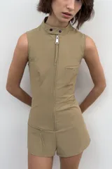 Mono corto entallado de cuello redondo y manga sisa, con cierre frontal de cremallera metálica y bolsillos delanteros con cremallera.