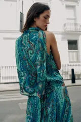 Top sin mangas de cuello alto con lazo ajustable, escote en V y diseño cruzado en el delantero. Presenta un estampado paisley en tonos verdes, azules y rosados, con bajo elástico y forro interior.