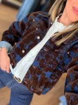 Campera corta de denim con diseño marmolado en tonos azul y marrón, con cierre frontal de botones metálicos y estructura clásica.