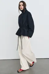 Parka de cuello alto con trabilla y manga larga, color azul marino. Presenta bolsillos laterales ocultos en la costura y cintura ajustable con cordón. El cierre frontal es con botones ocultos por solapa.